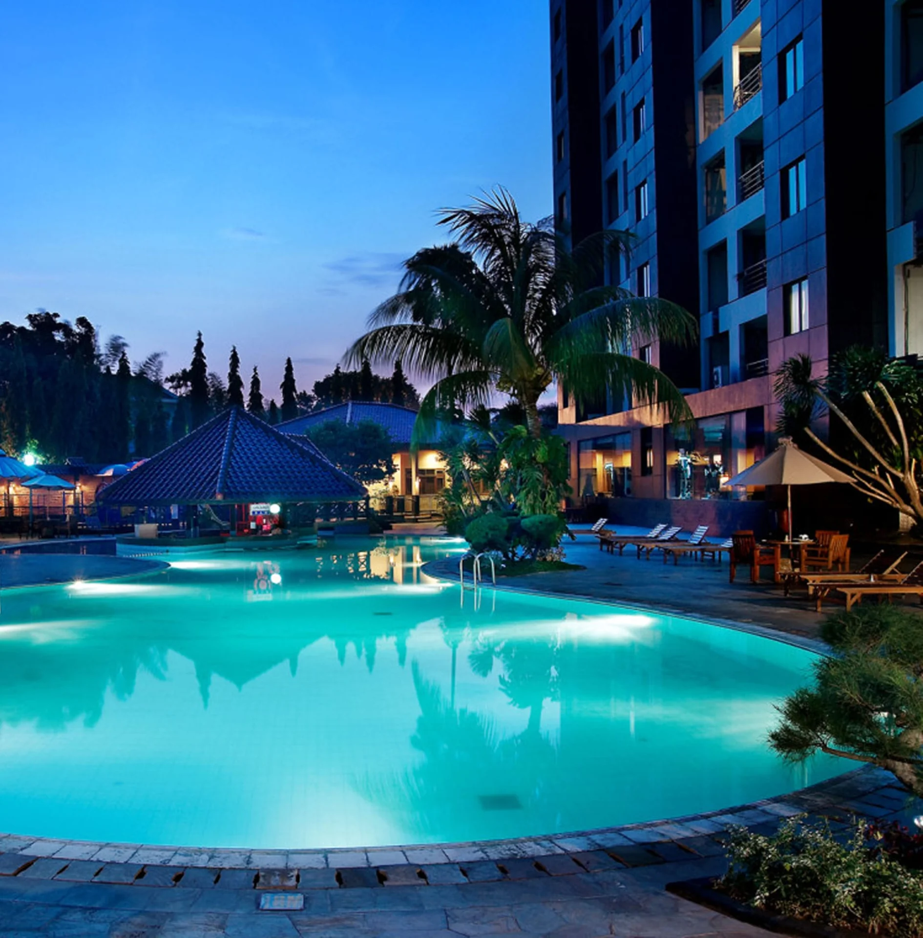 Kolam renang outdoor Hotel Kristal Jakarta saat senja dengan lampu bawah air dan kursi berjemur