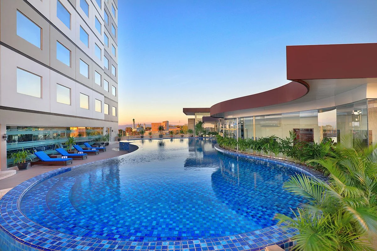 kolam renang outdoor Aston Kupang dengan kursi santai biru dan tanaman palem di lantai 3