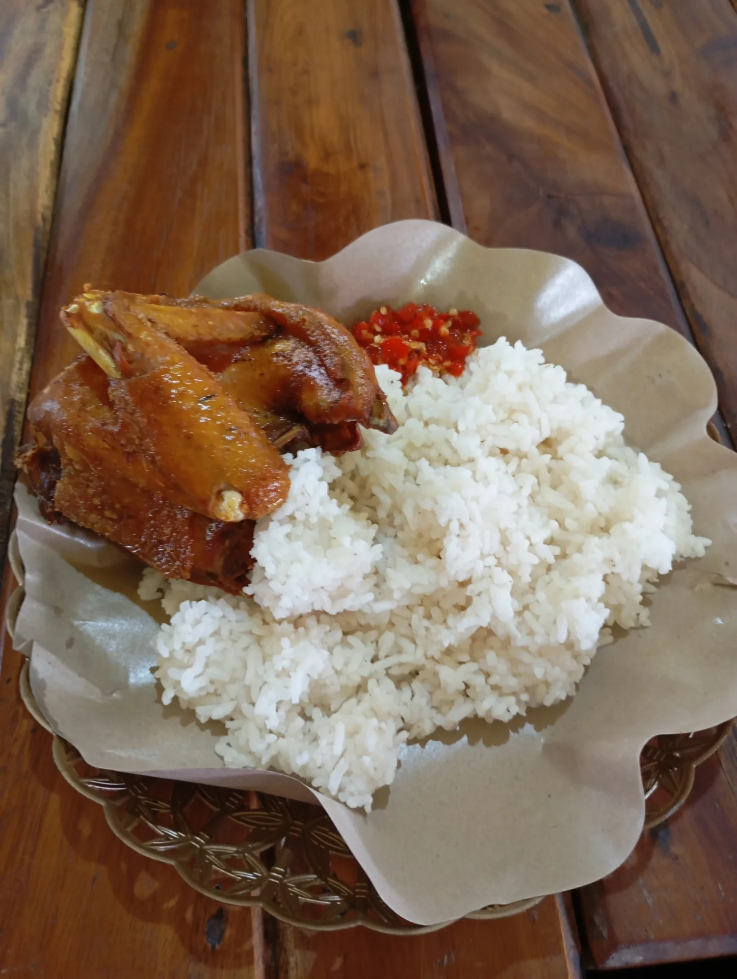 ayam kampung goreng berkulit cokelat keemasan dengan nasi putih dan sambal merah di atas kertas nasi