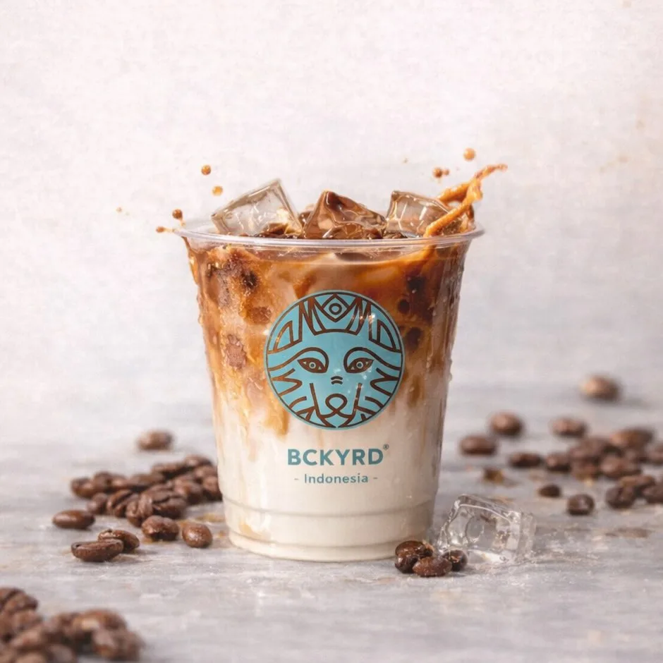 Es kopi susu dalam gelas plastik berlogo BCKYRD dengan biji kopi