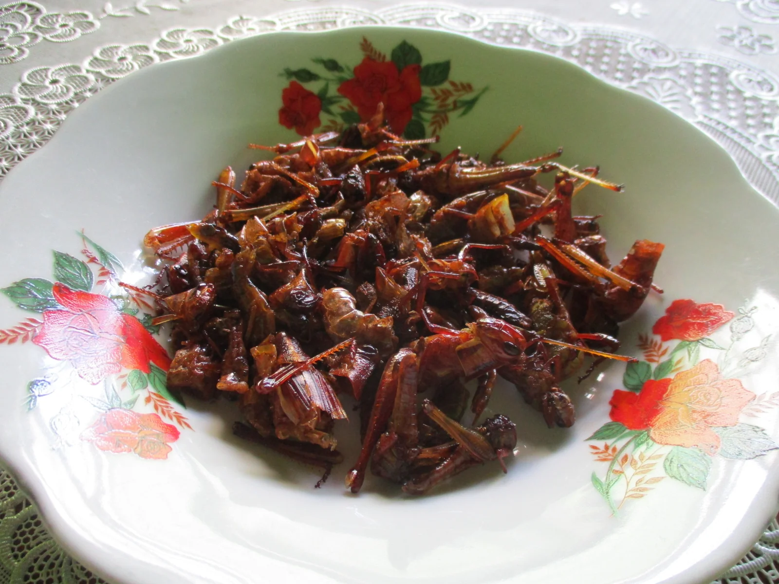 Belalang goreng kecokelatan dengan kaki masih utuh di atas piring