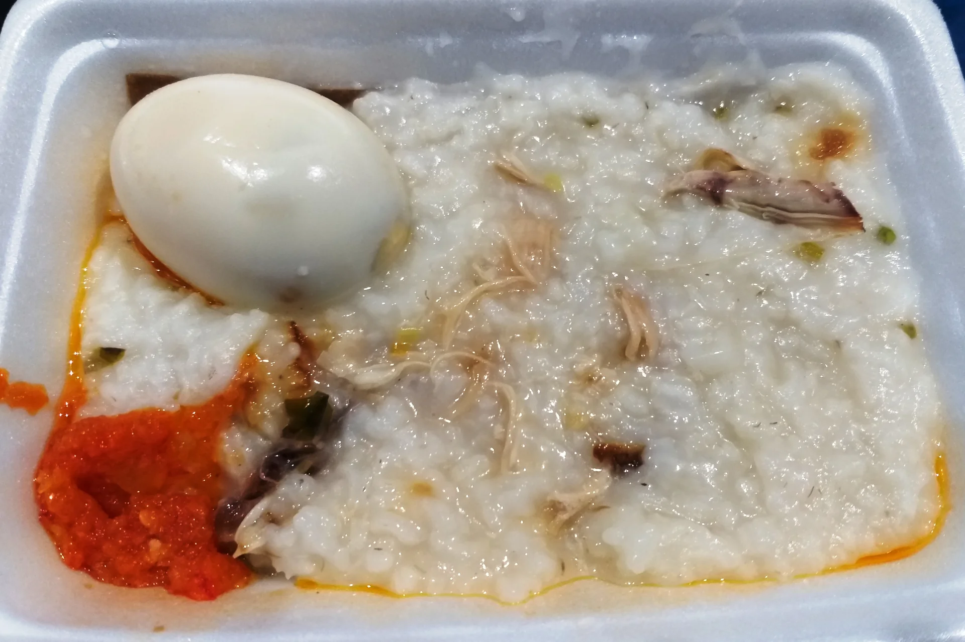 bubur ayam dengan suwiran ayam, telur rebus, dan sambal merah dalam wadah styrofoam