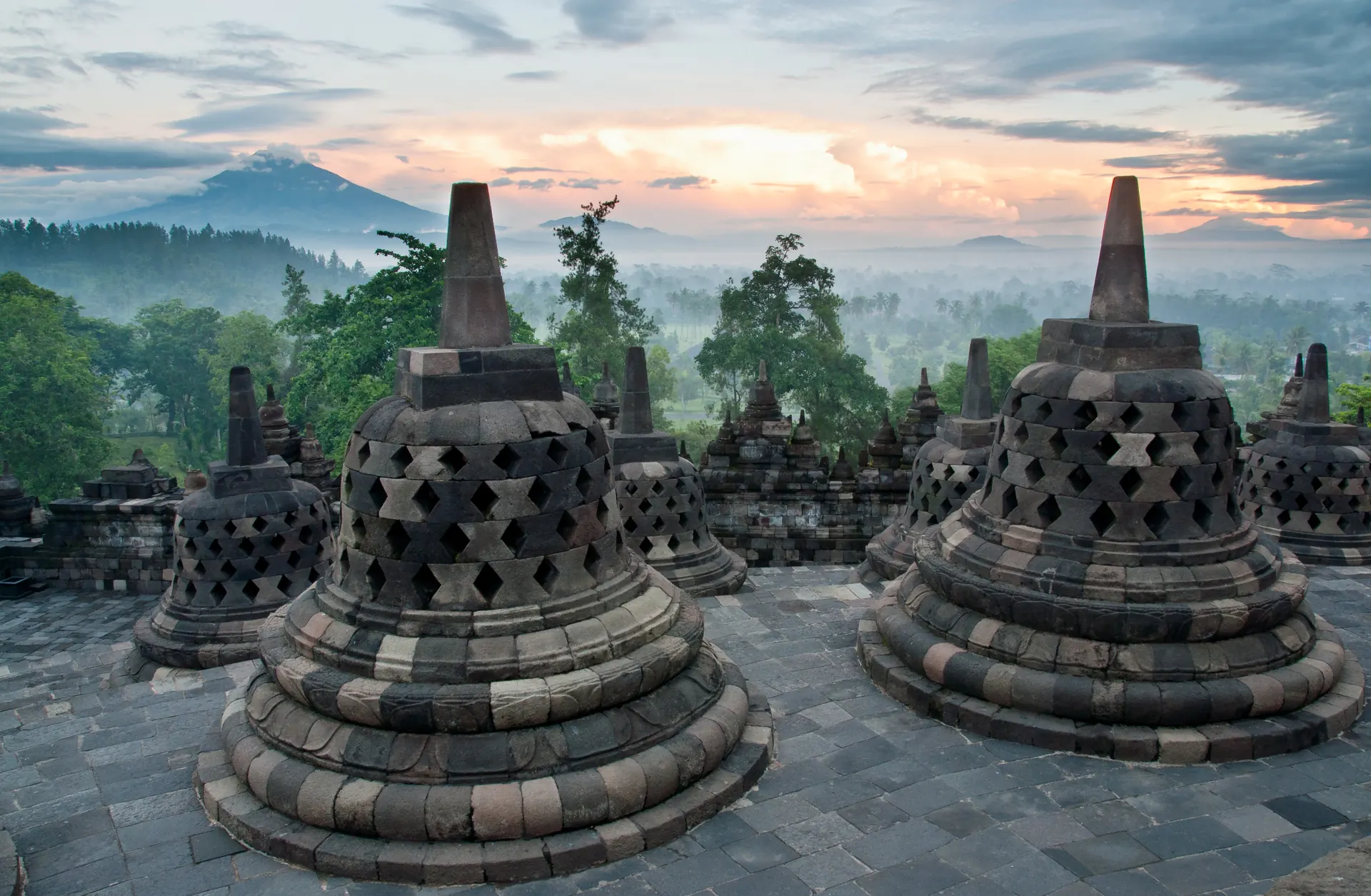 Stupa berlubang di teras atas Candi Borobudur dengan kabut pagi dan Gunung Merapi di kejauhan