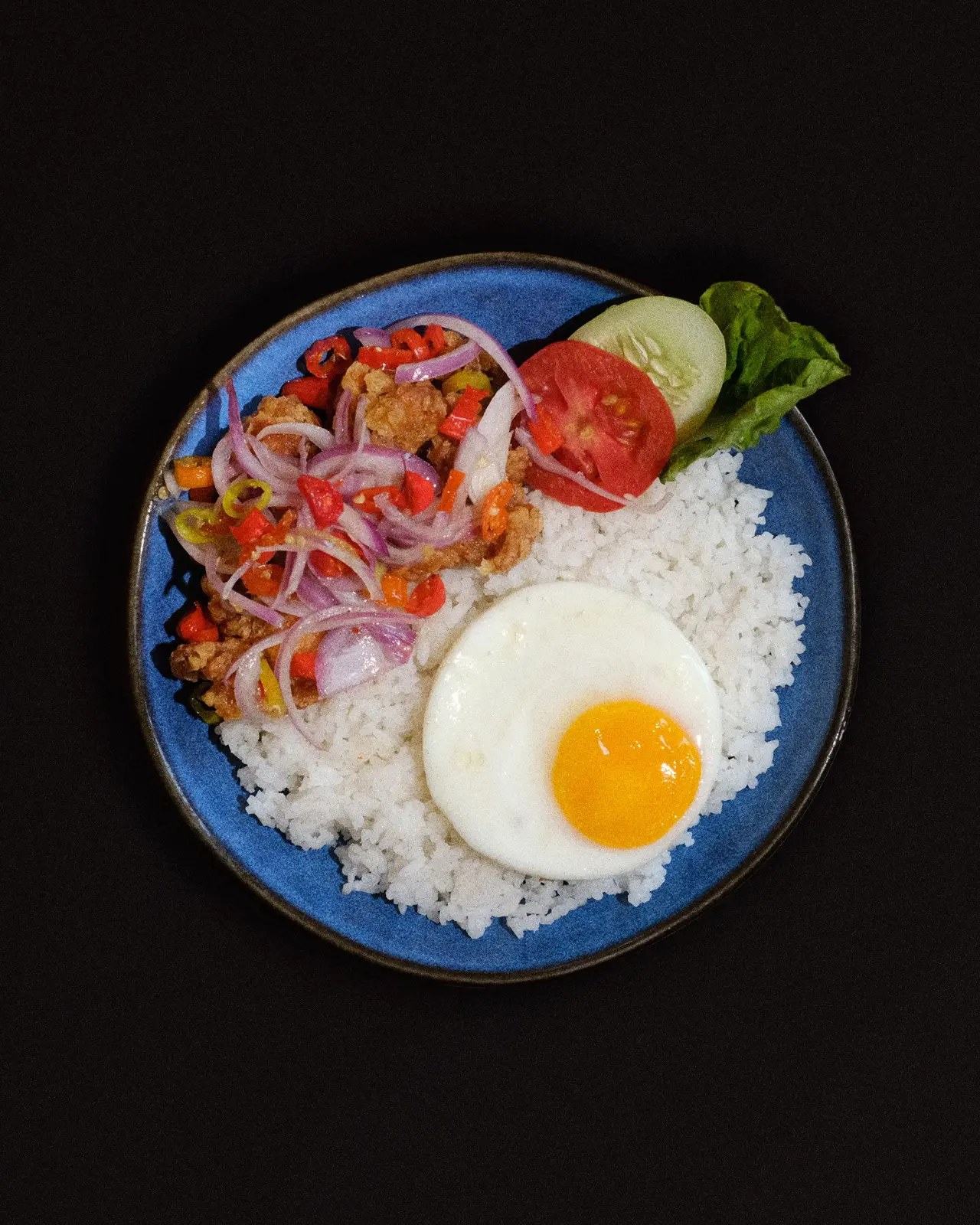 Sepiring nasi dengan telur ceplok dan salad di piring biru