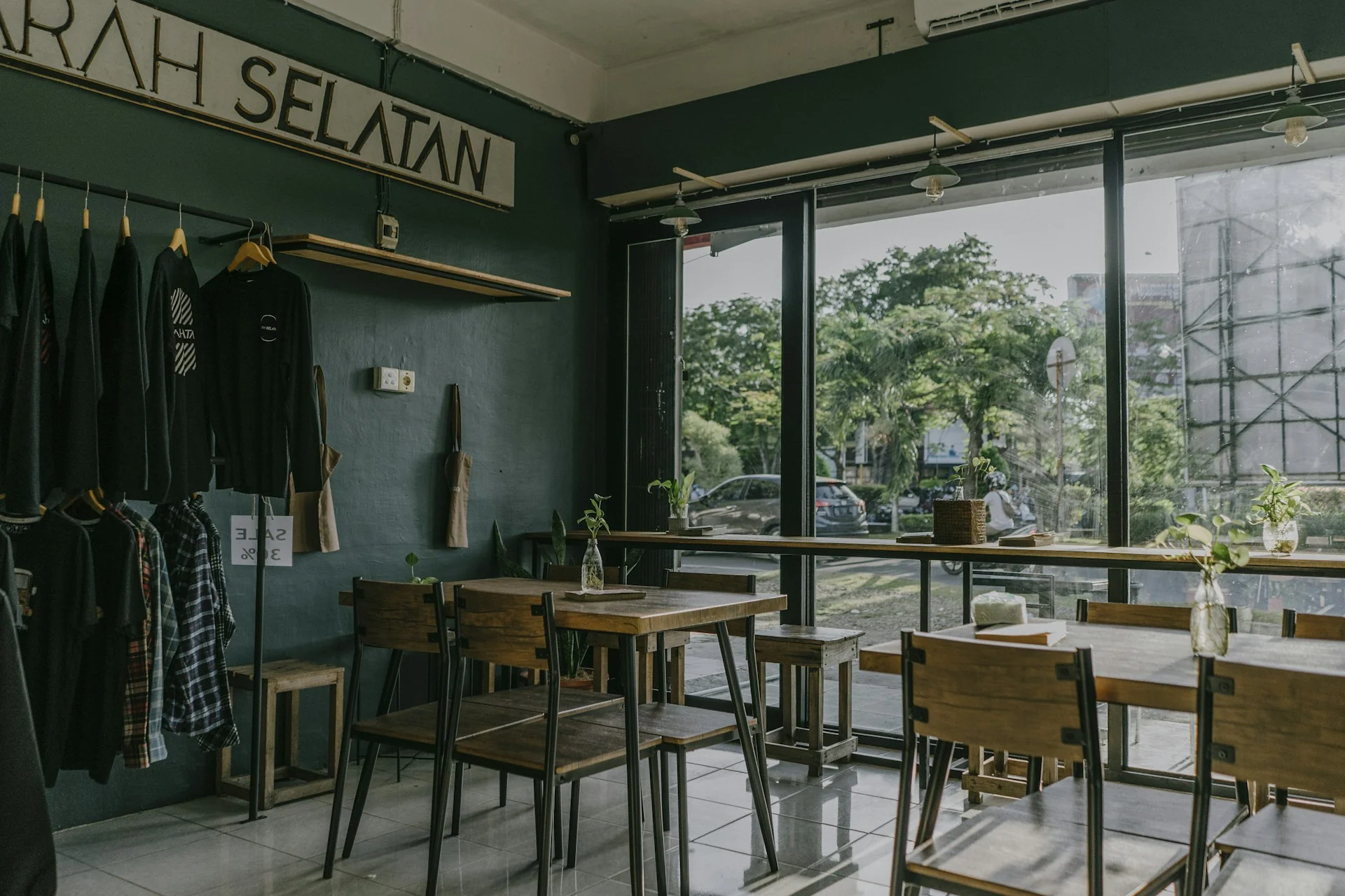 Interior kedai kopi dengan meja kayu, bar menghadap jendela kaca, dan stopkontak di dinding hijau tua
