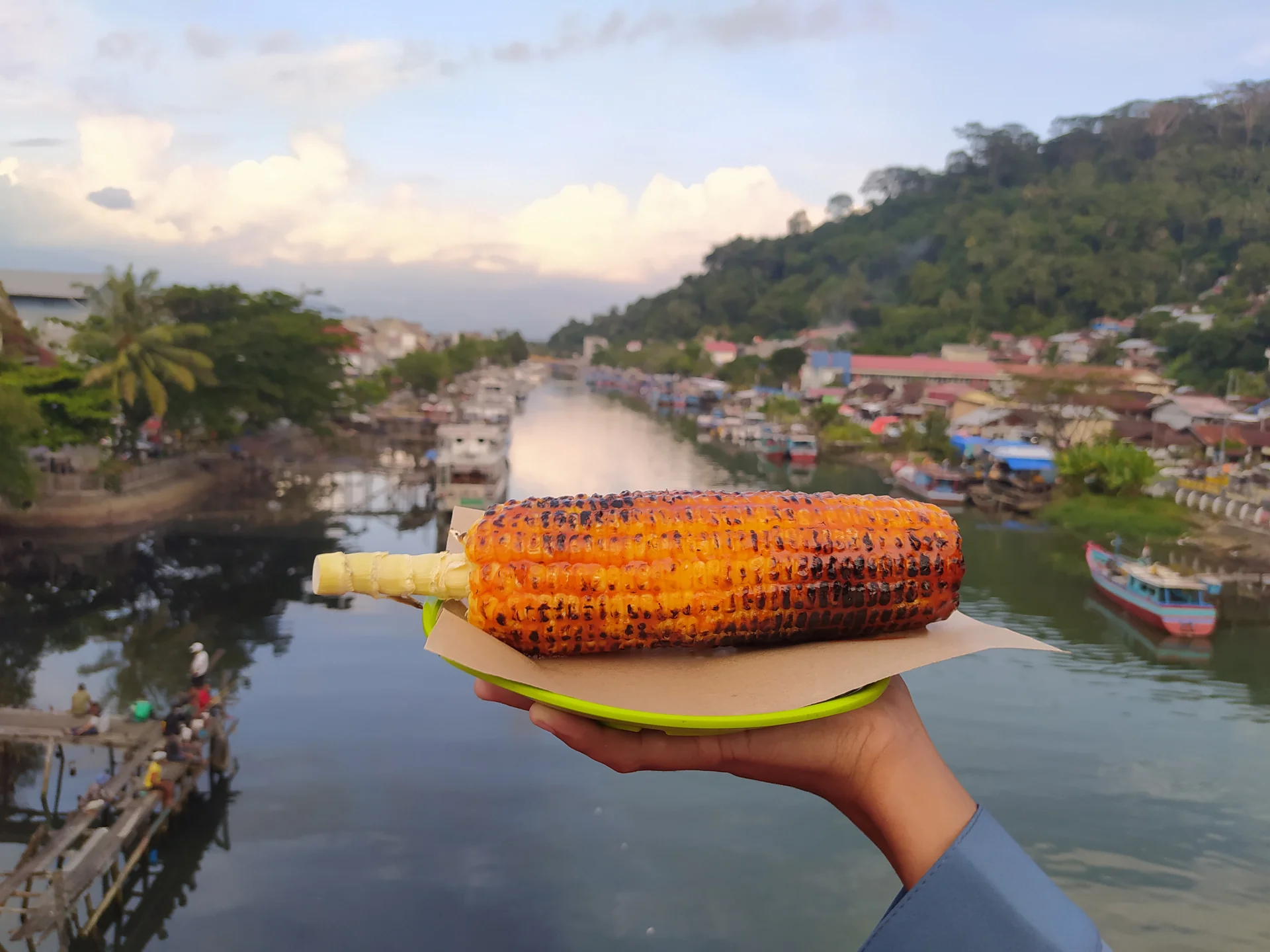 Jagung bakar dipegang di atas Jembatan Siti Nurbaya dengan latar Sungai Batang Arau