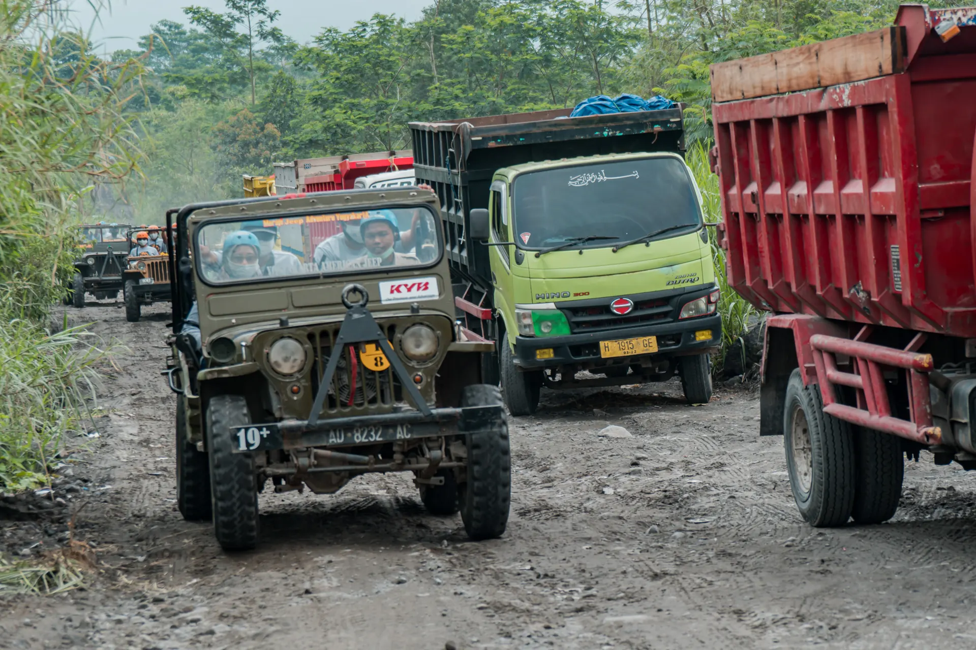 Jip wisata dan truk pasir berpapasan di jalan tanah berdebu lereng Merapi dekat Kaliadem, Kaliurang, Sleman