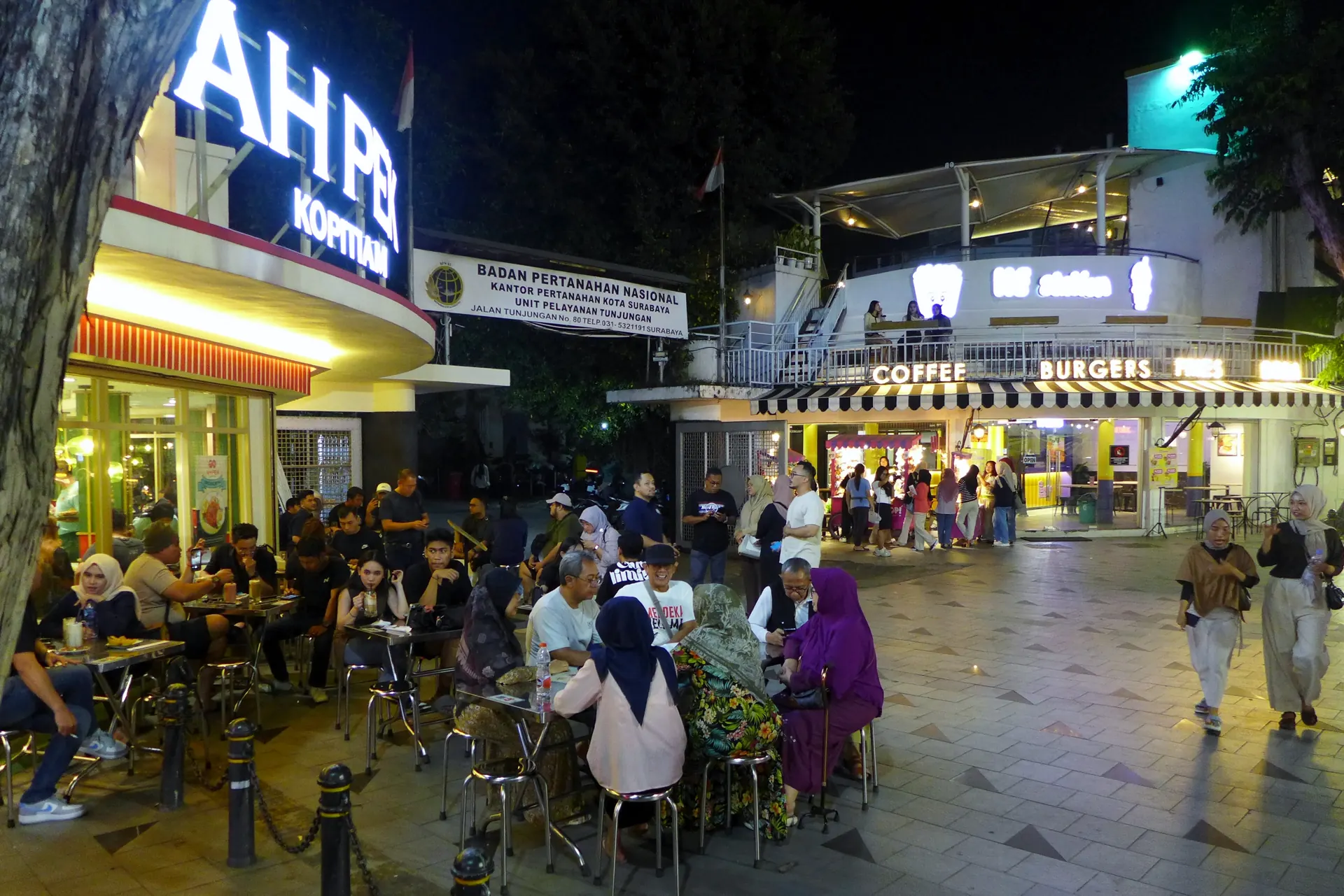 Pengunjung duduk di meja luar kopitiam di trotoar Jalan Tunjungan Surabaya pada malam hari
