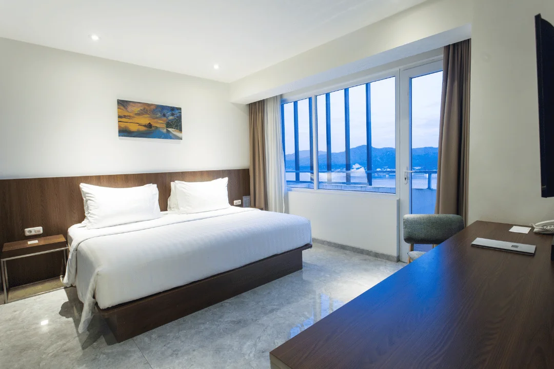Kamar Hotel Santika Premiere Ambon dengan ranjang putih dan jendela lebar menghadap Teluk Ambon