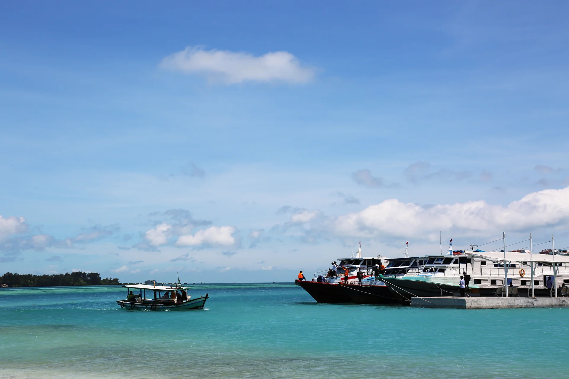 kapal motor penumpang bersandar di dermaga Pulau Harapan, Kepulauan Seribu, dengan perahu kayu kecil melintas di laut biru