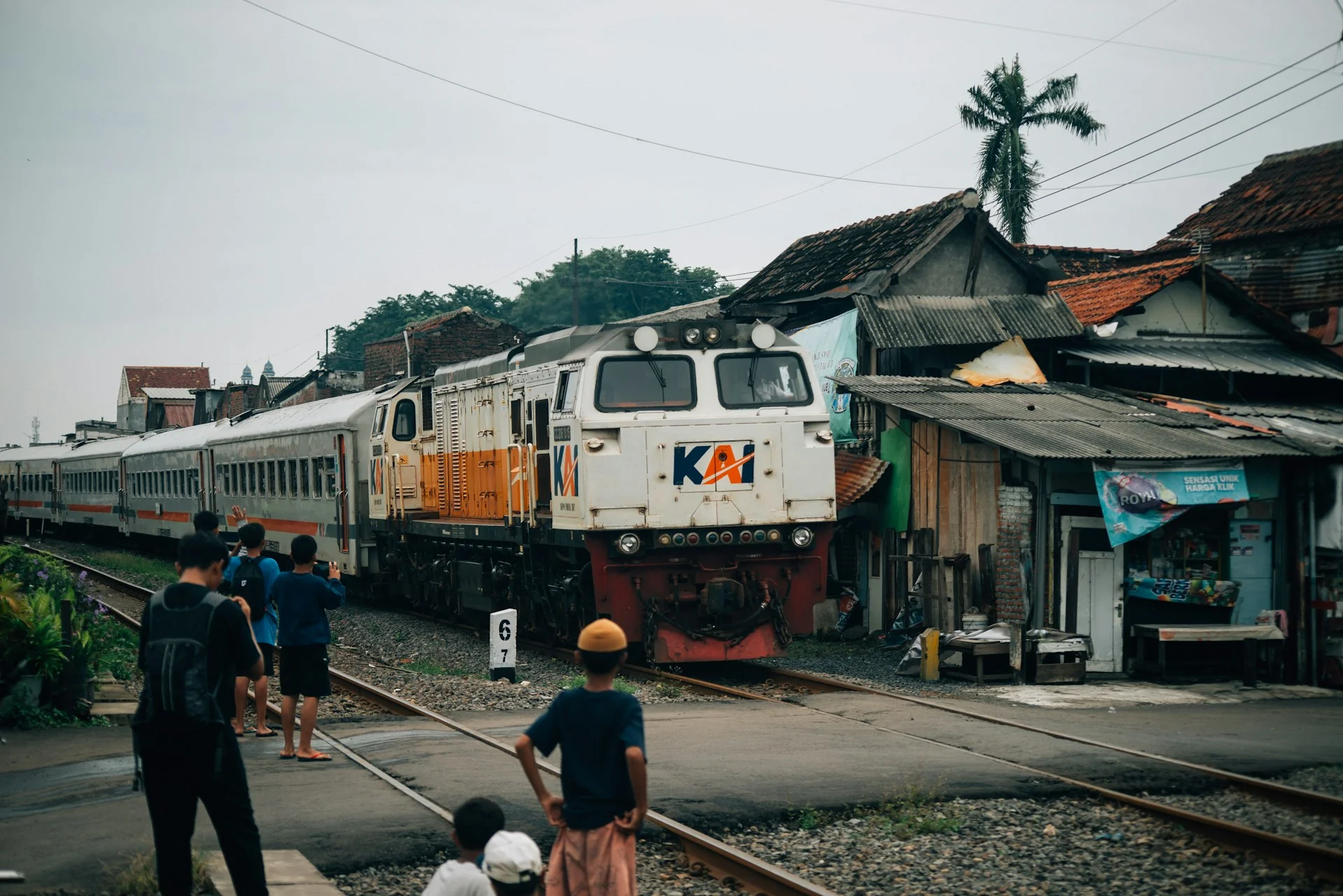 Lokomotif KAI menarik rangkaian kereta penumpang mendekati Stasiun Wonokromo, Surabaya, disaksikan warga di tepi rel