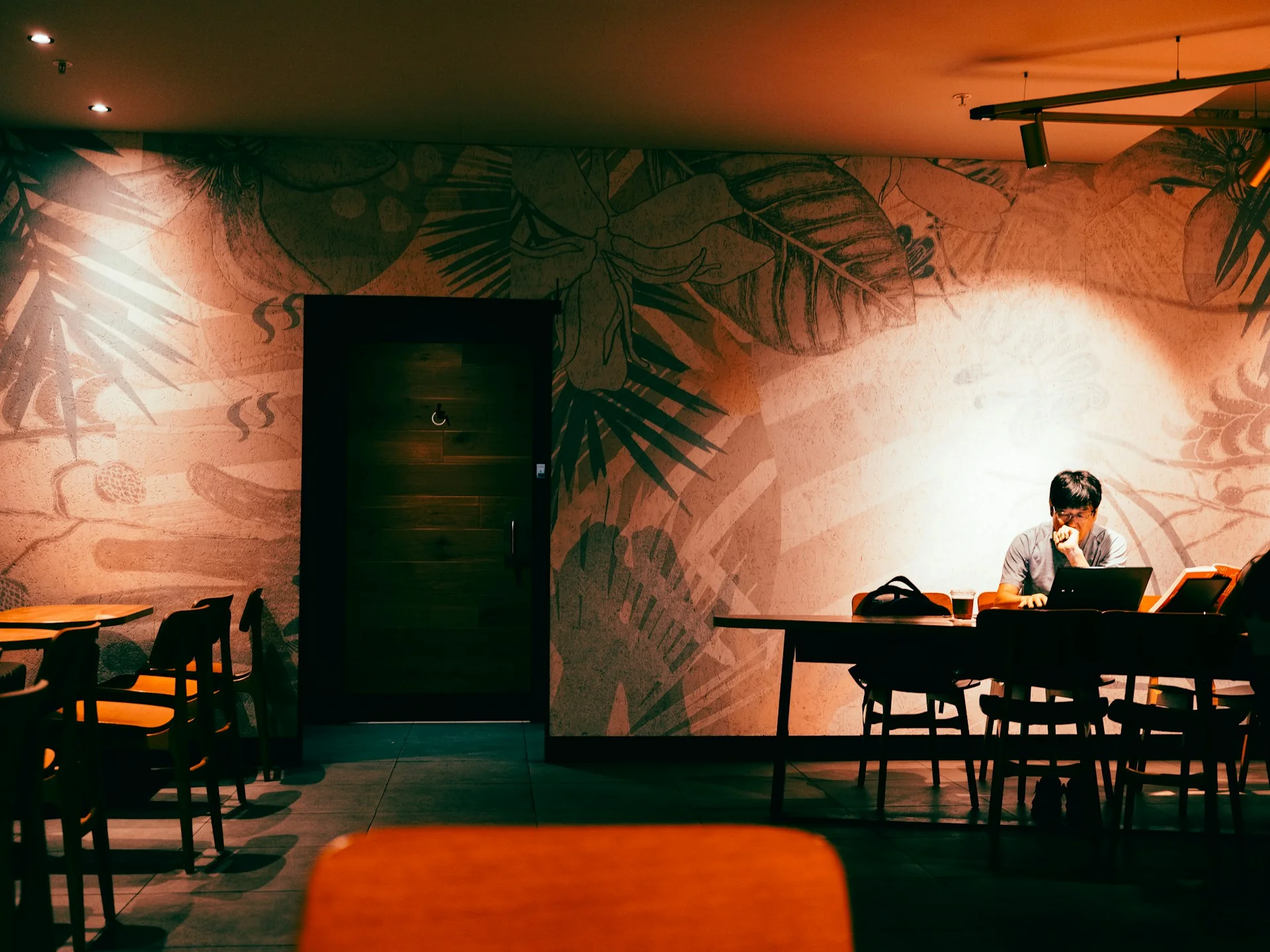 Seorang pria bekerja dengan laptop di kafe berpencahayaan redup pada malam hari