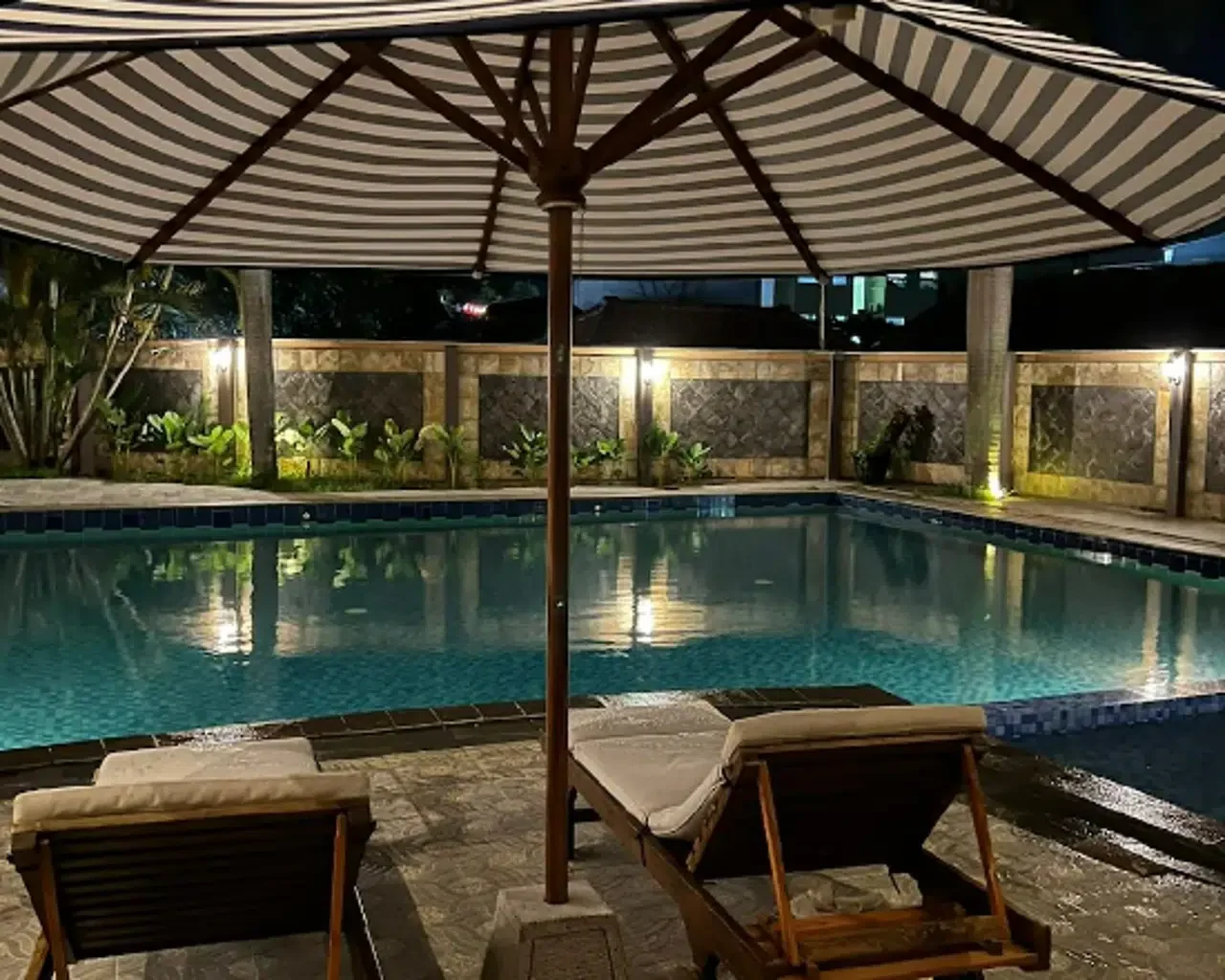 Kolam renang Hotel Grand Situ Buleud pada malam hari dengan dua kursi berjemur di bawah payung