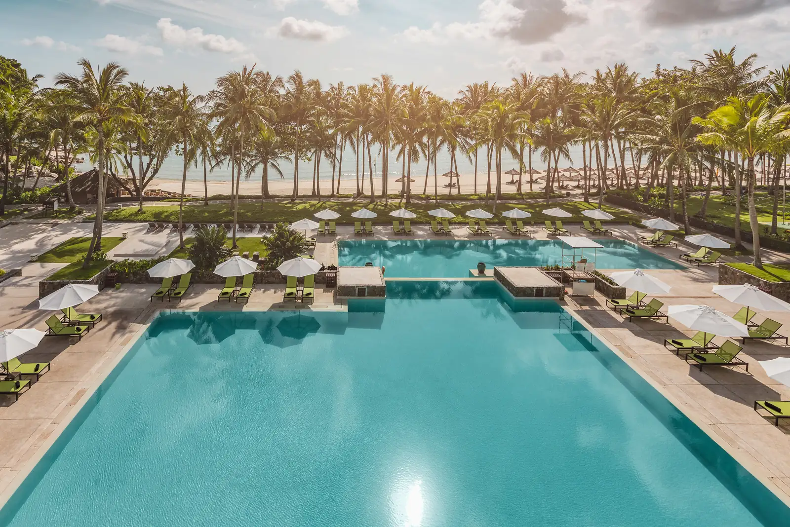 kolam renang dua tingkat berlatar deretan pohon kelapa dan pantai di Club Med Bintan Island