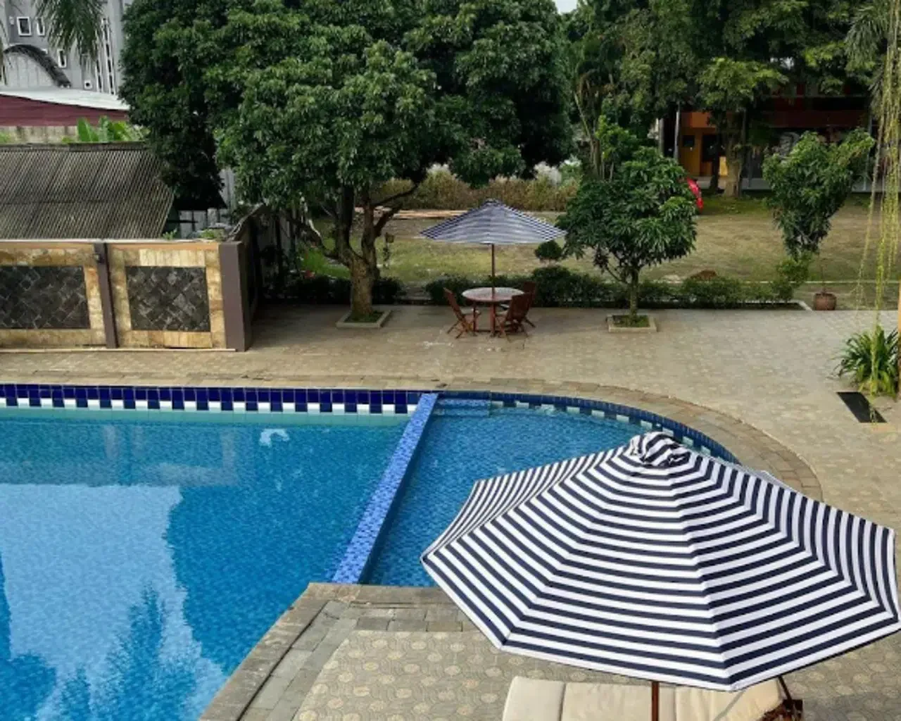 Kolam renang outdoor Hotel Grand Situ Buleud Purwakarta dengan payung bergaris di siang hari