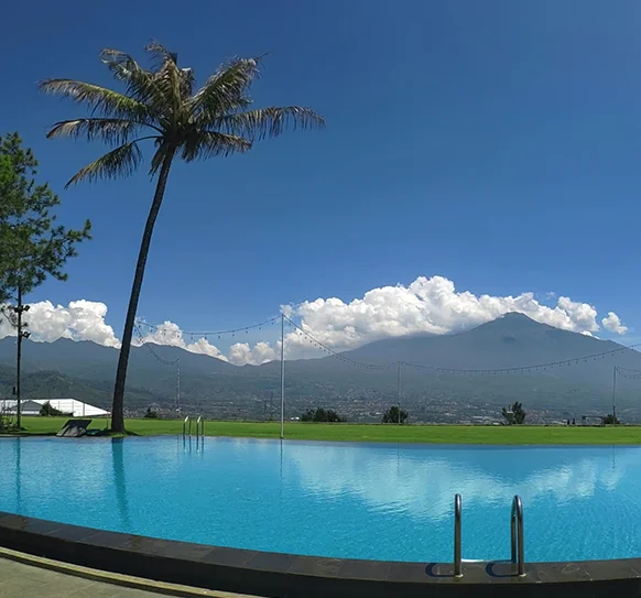 kolam renang Kusuma Agrowisata Resort Batu menghadap deretan gunung dan pohon kelapa