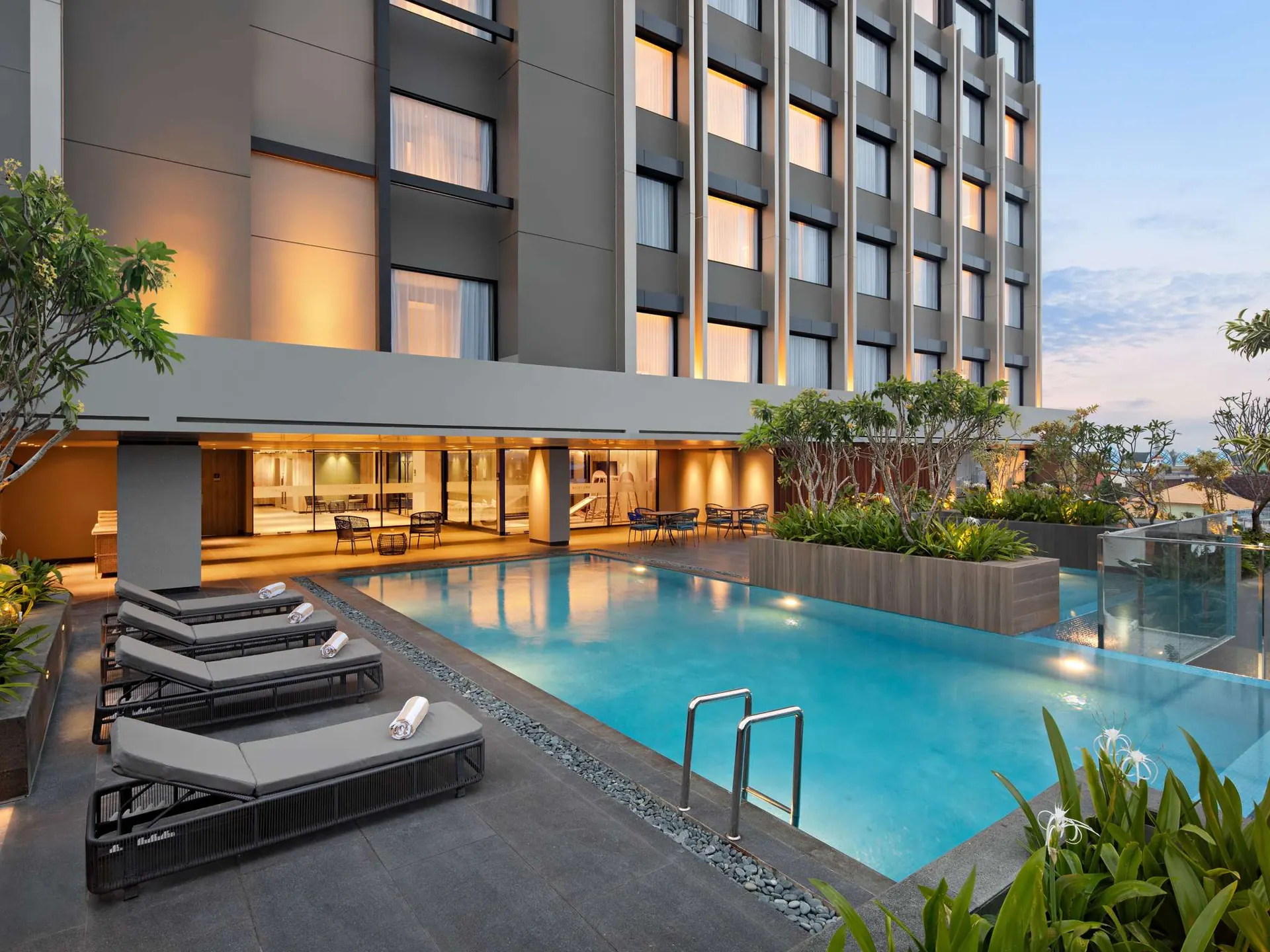 kolam renang outdoor Mercure Madiun dengan kursi berjemur abu-abu di depan gedung hotel