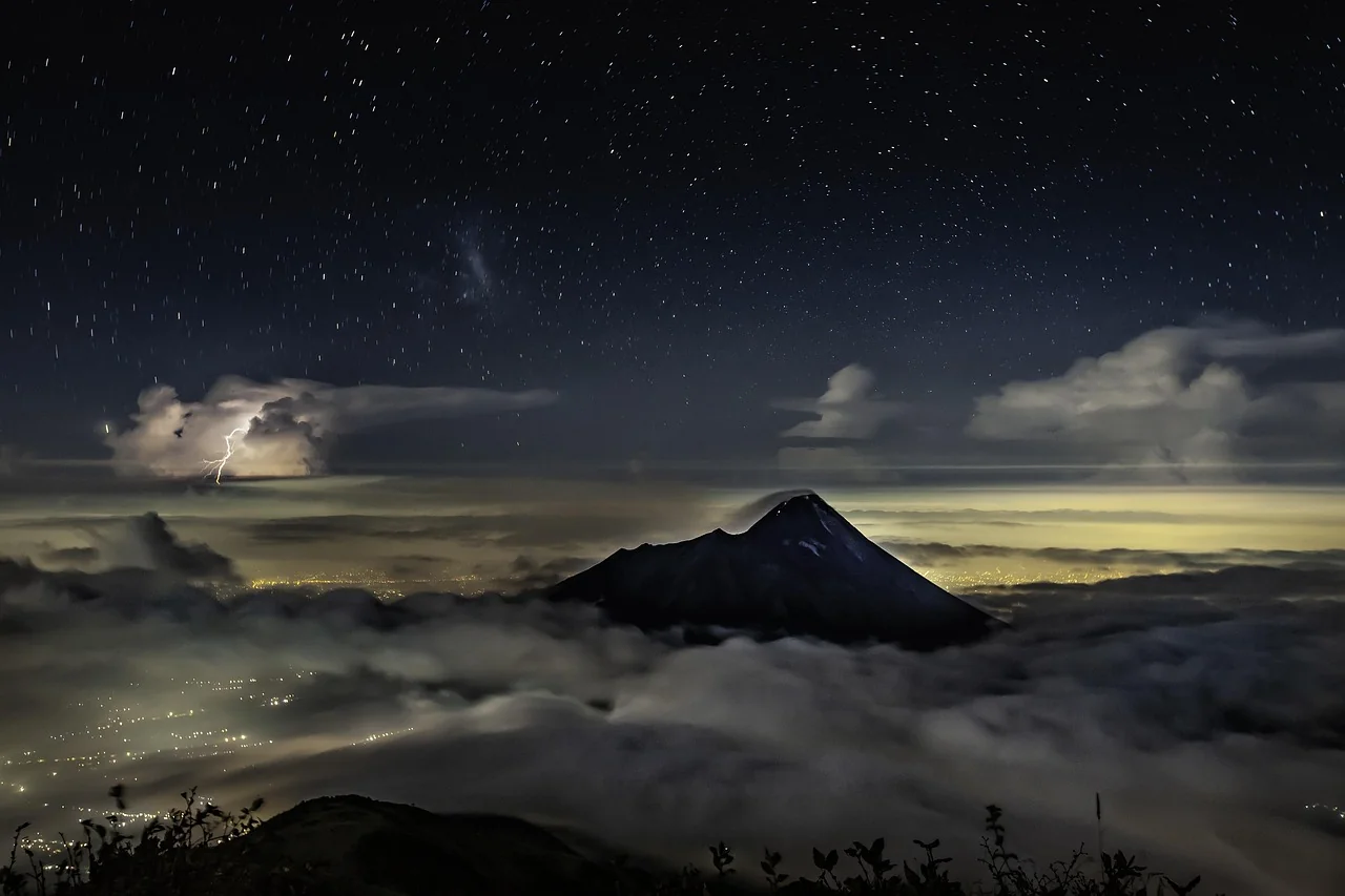 Gunung Merapi di malam berbintang di atas lautan awan dengan cahaya lampu kota Yogyakarta di kejauhan