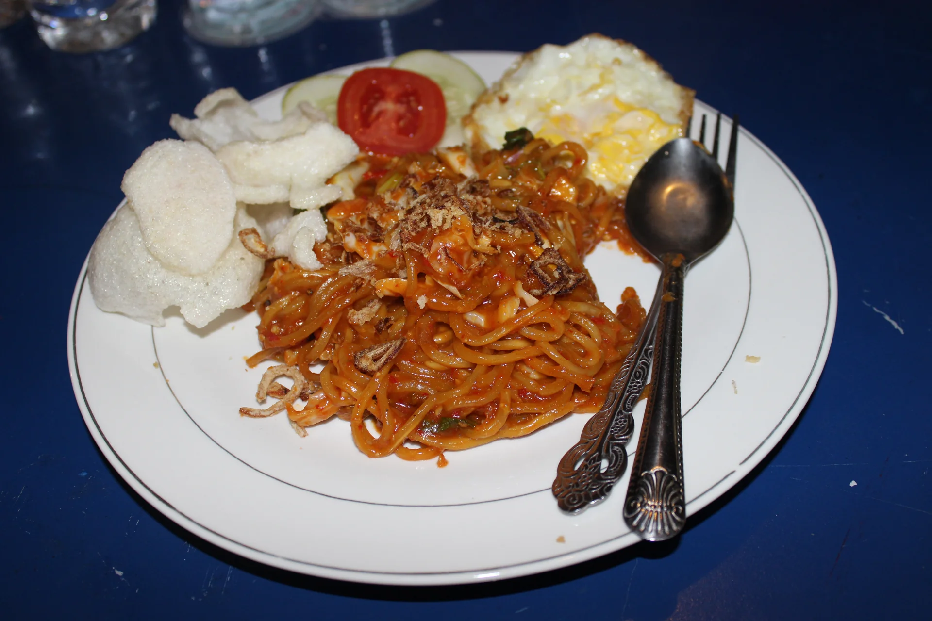 Sepiring mi Aceh goreng berbumbu merah dengan telur mata sapi, kerupuk, irisan tomat, dan mentimun