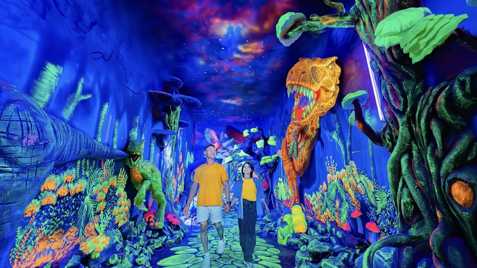 Pengunjung berjalan di lorong bercahaya neon bertema dinosaurus di Milenial Glow Garden, Jatim Park 3
