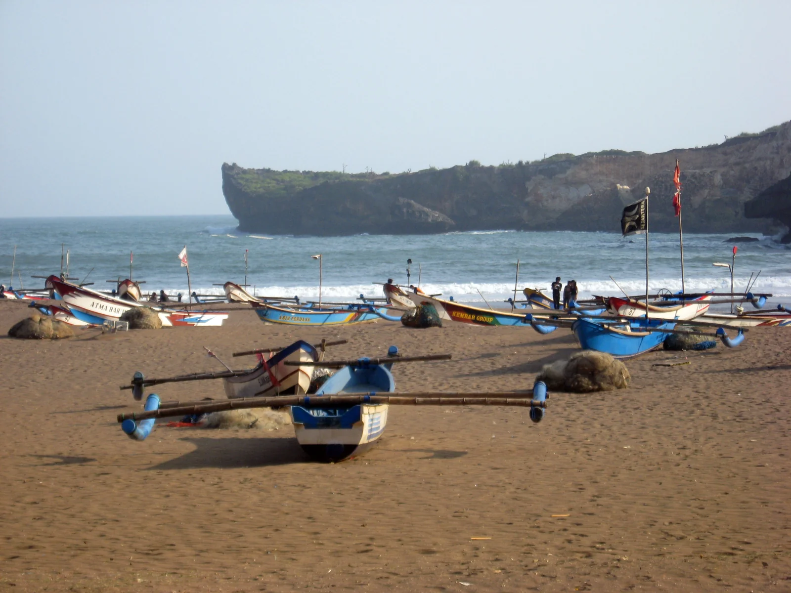 Perahu nelayan biru putih di pasir Pantai Baron dengan tebing karang
