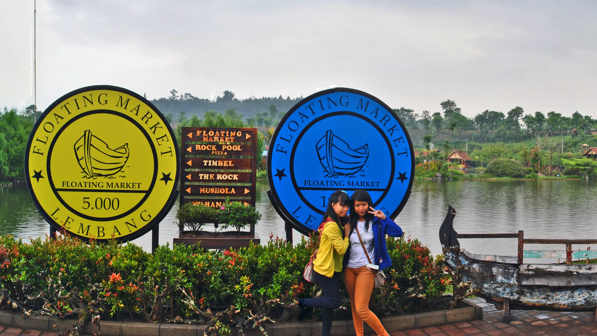 Papan berbentuk koin bertulisan Floating Market Lembang dan penunjuk arah di tepi danau