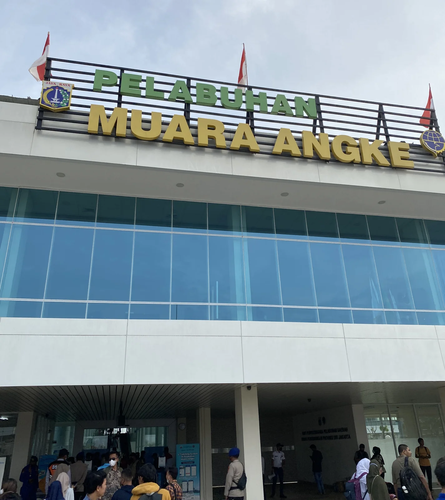 gedung terminal penumpang Pelabuhan Muara Angke di Jakarta Utara dengan papan nama besar dan calon penumpang di pintu masuk