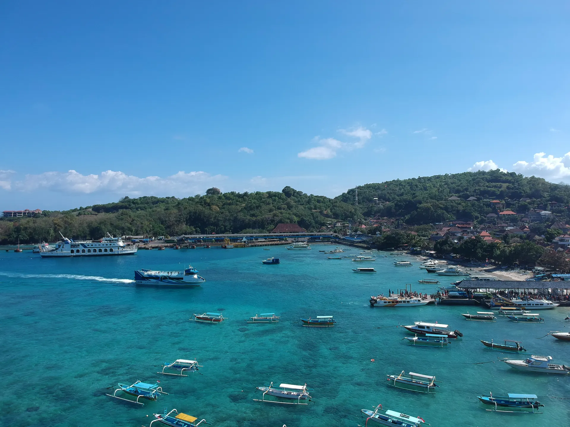 Teluk Pelabuhan Padang Bai, Karangasem, dengan kapal feri roro bersandar, fast boat melaju, dan perahu jukung di air biru