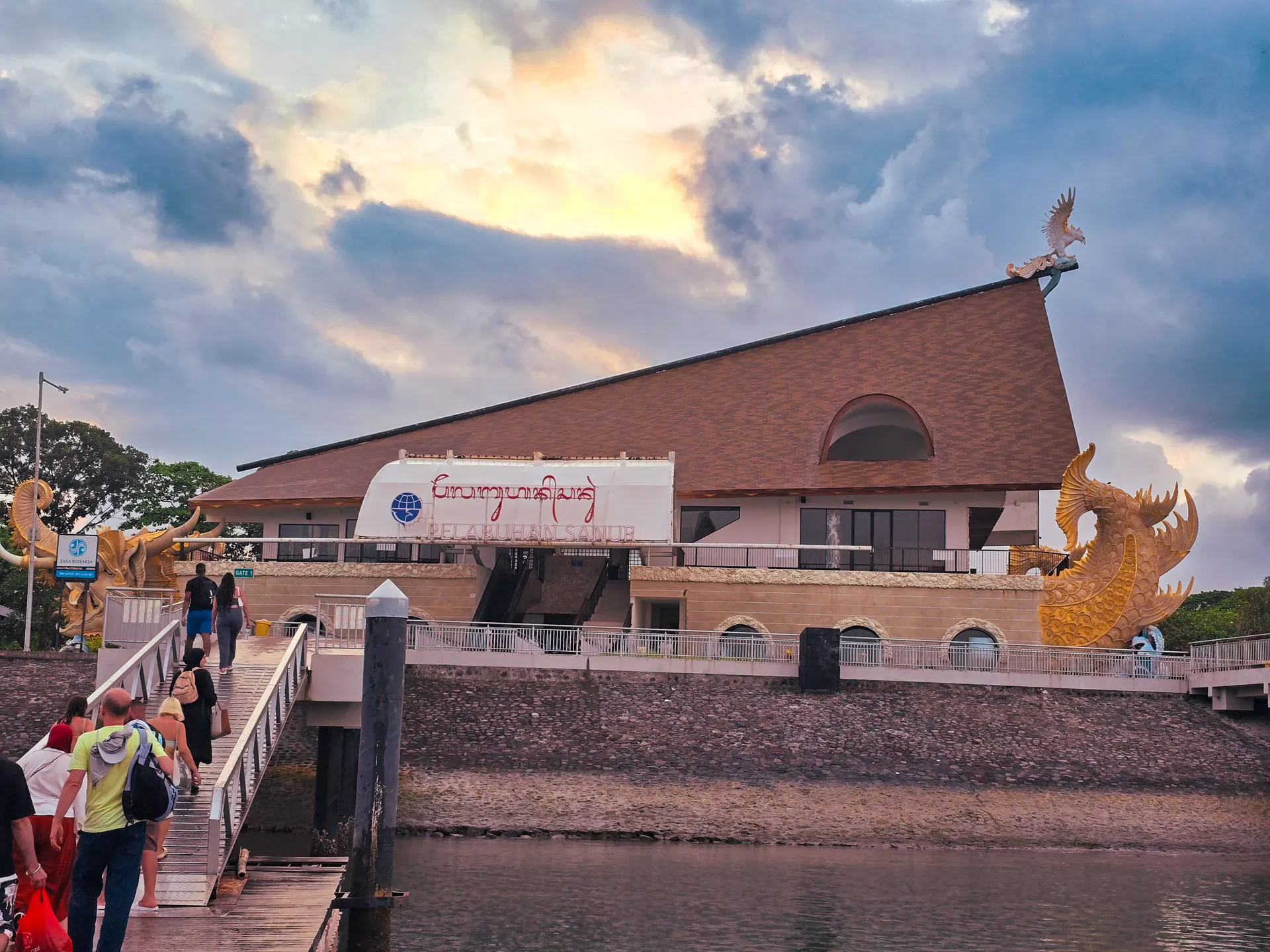Penumpang berjalan di jembatan dermaga menuju gedung terminal Pelabuhan Sanur, Denpasar, saat senja