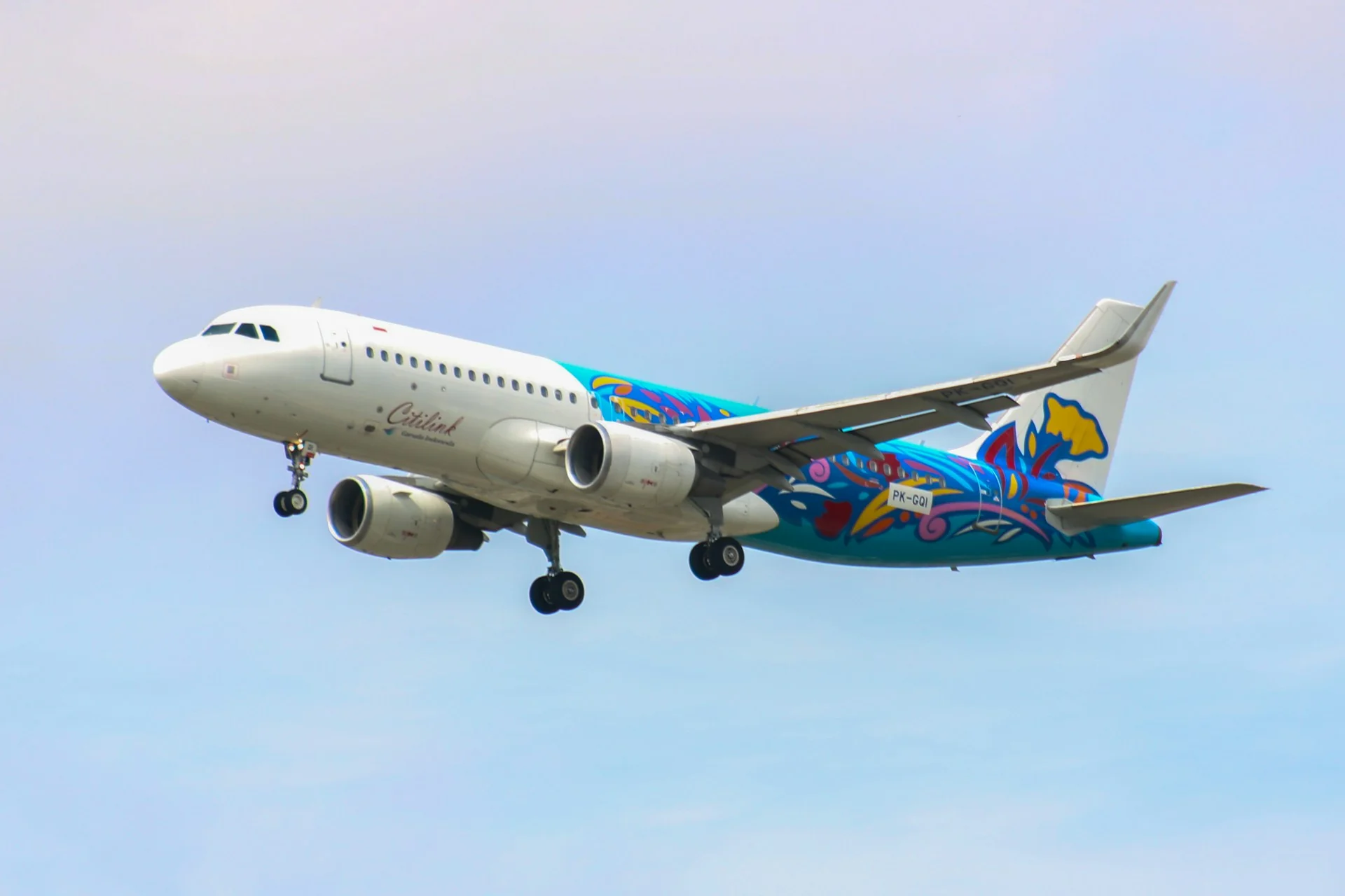 Pesawat Airbus A320 Citilink bercorak batik warna-warni terbang dengan roda pendarat terbuka di langit biru