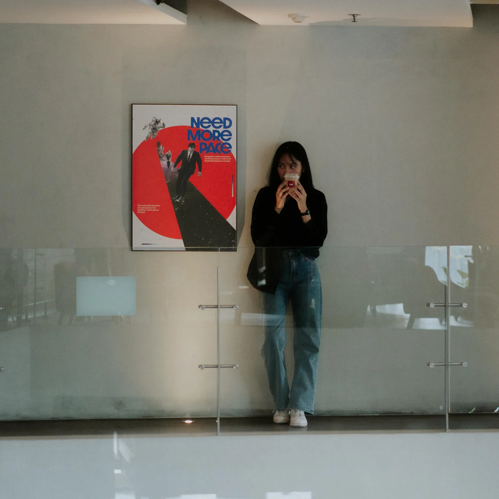 Pengunjung berdiri di depan dinding putih dengan poster merah di Saé Coffee