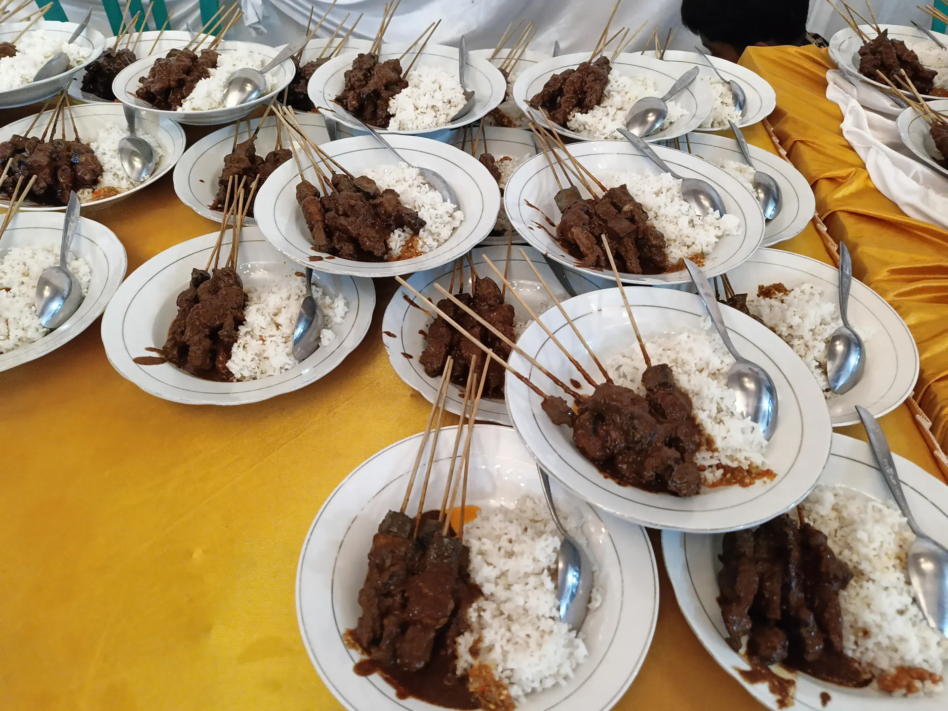 piring-piring sate kambing berbumbu kecap dengan nasi putih tertata di meja bertaplak kuning