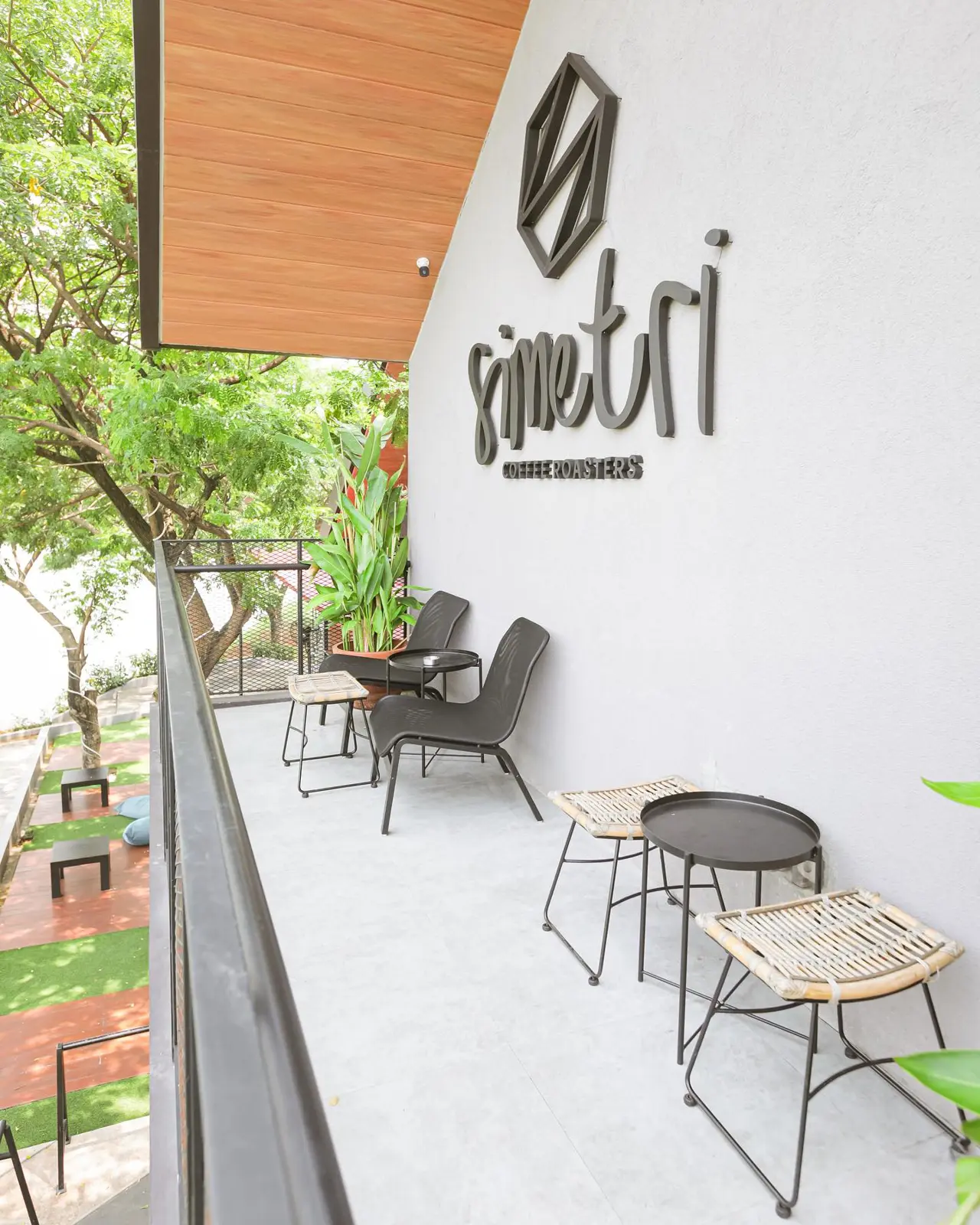 Teras Simetri Coffee Roasters dengan kursi rotan dan logo di dinding