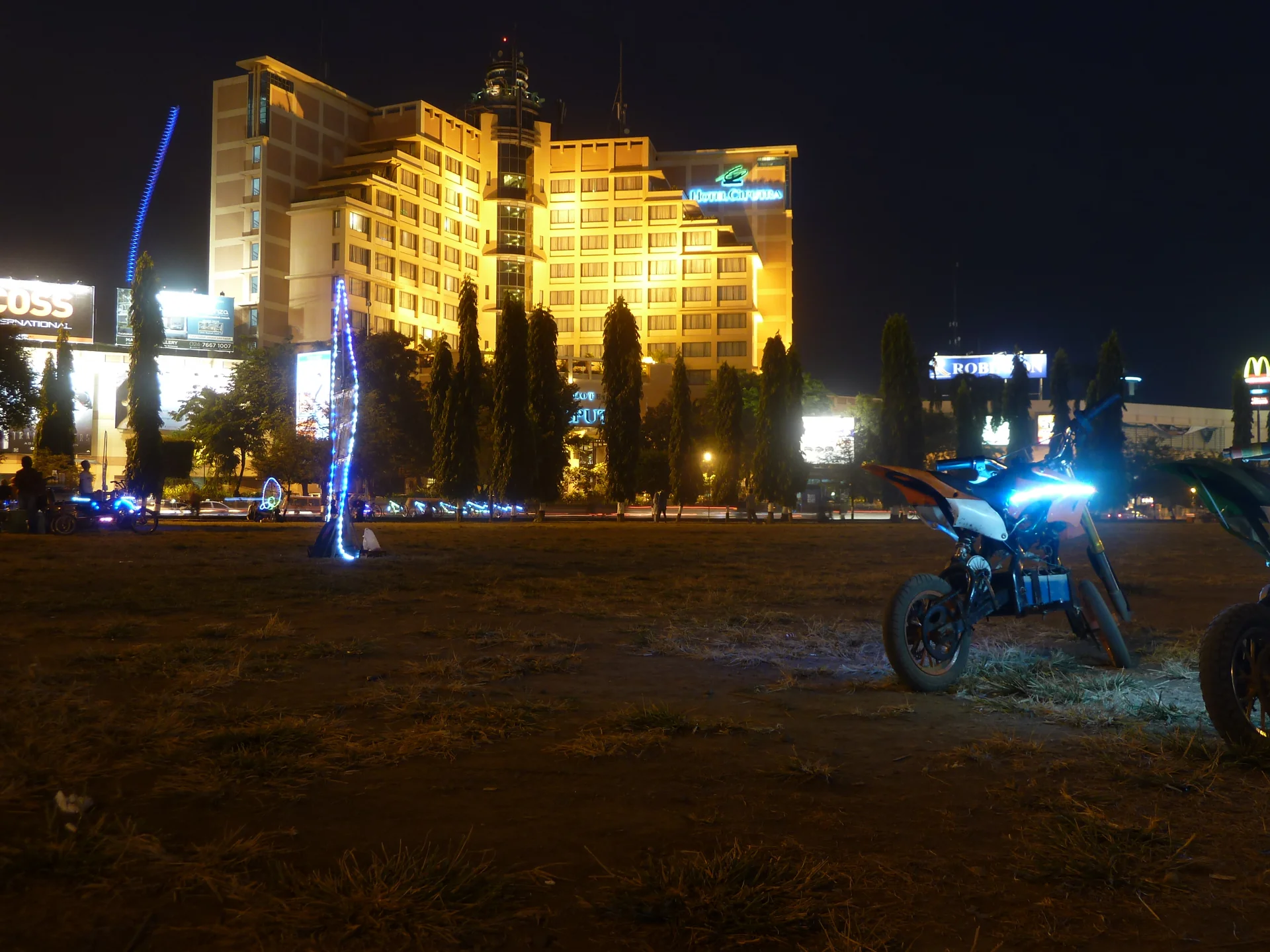 Lapangan Pancasila Simpang Lima Semarang pada malam hari dengan sepeda motor mini berlampu di rumput dan gedung Hotel Ciputra yang terang di latar belakang