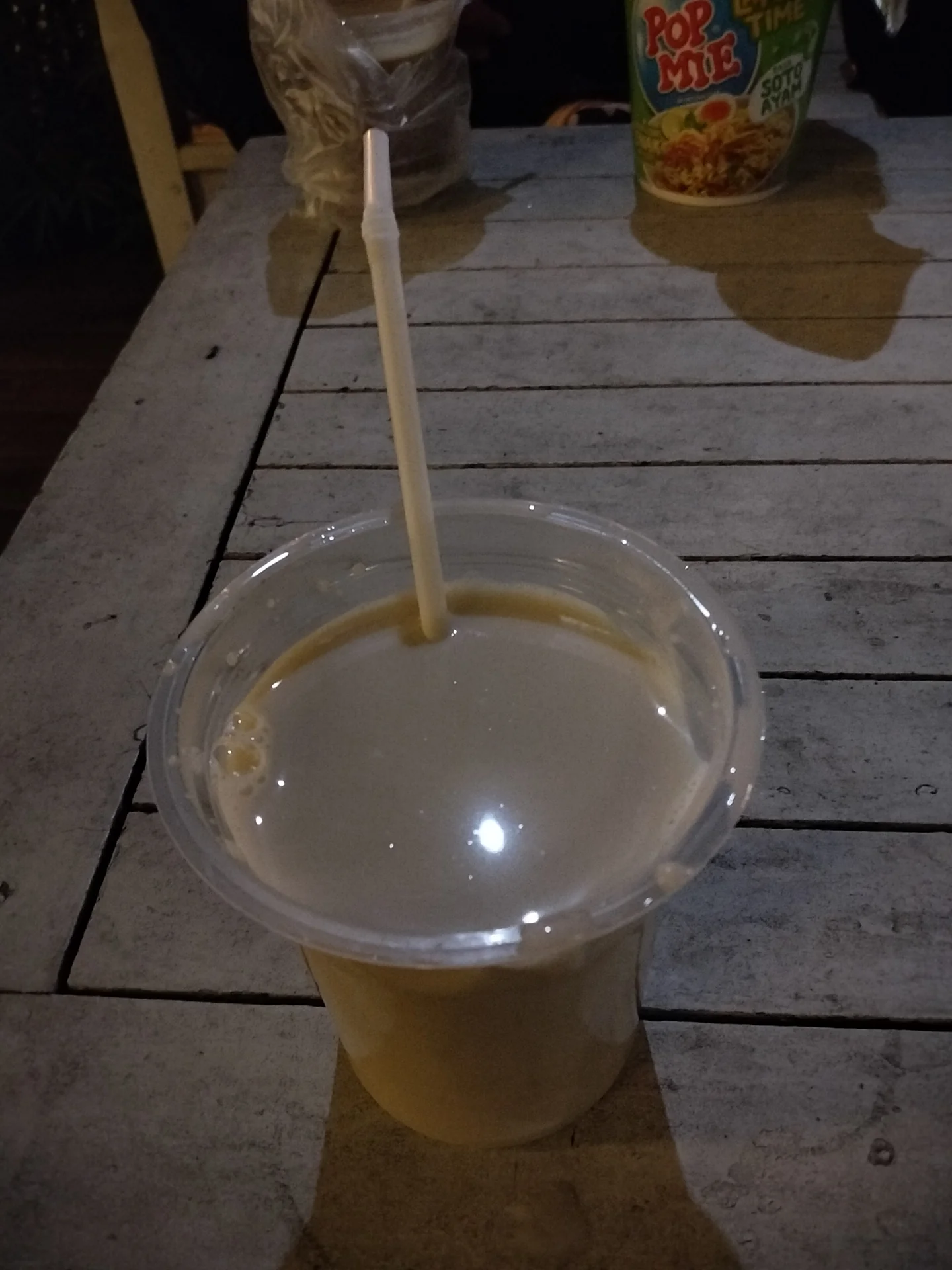 Segelas STMJ hangat dengan sedotan di meja kayu area kuliner Batu Night Spectacular pada malam hari