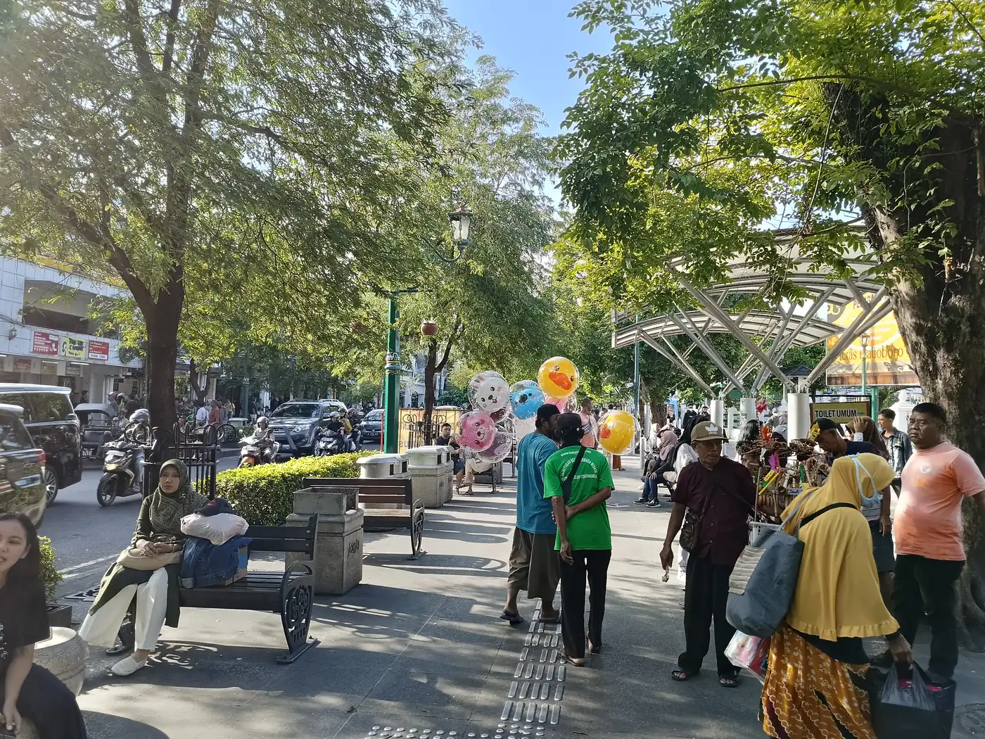 Pengunjung berjalan dan duduk di bangku trotoar Malioboro, Yogyakarta, yang teduh oleh pepohonan pada siang hari